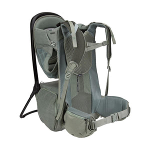 Sage green baby backpack by Thule with a black frame, mesh back panel, and hip belt pockets, shown from a side view.