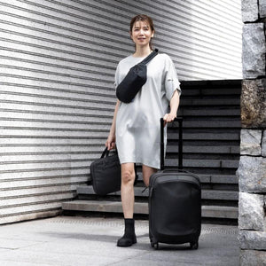 Black laptop and tablet attache by Thule, carried by a woman also wearing a black fanny pack and pulling black rolling luggage.