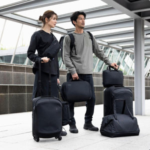 Black 14-inch laptop and tablet attache by Thule, held by a man in a modern travel environment with other black luggage.