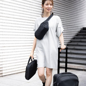 Black 16-inch laptop and tablet attache by Thule, held by a woman walking with rolling luggage and a sling bag.