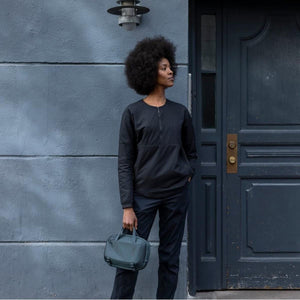 Dark grey crossbody bag by Thule, held by a woman wearing a black jacket, outdoors.