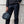 Dark teal crossbody bag by Thule, held by a person in a black jacket and dark pants.