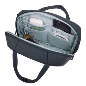 Dark gray/blue crossbody bag by Thule, open showing organizational pockets containing earbuds, phone, keys, and charging cable.