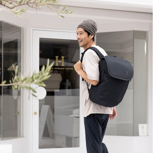 Black 26L travel backpack by Thule, worn by a smiling man walking past a coffee shop.