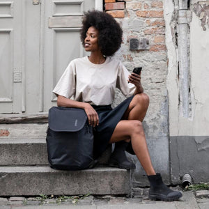 Black roll-top backpack by Thule, sitting on stone steps beside a woman in a beige top.