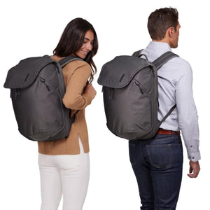 Dark grey 26L backpack by Thule, shown worn by a man and woman, featuring a flap closure and front zip pockets.