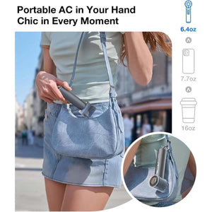 Charcoal handheld fan with ice cooler by Torras, carried by a woman with a light blue denim bag, showcasing its compact size and hanging option.