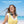 Dark gray portable neck fan by Torras with a mesh grille, worn by a smiling woman in a yellow top at a sunny beach.