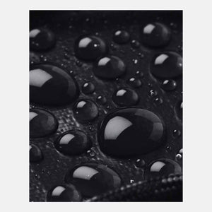 Black small backpack by Under Armour, showing a water-repellent textured surface with many dark water droplets.