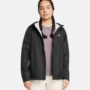 Black hooded jacket by Under Armour with a white logo, worn open over a purple shirt and beige pants.