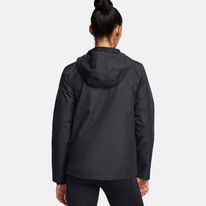 Black women's lined rain jacket by Under Armour, seen from the back with the hood up, worn with black leggings.