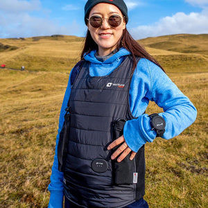 Black padded waterproof diving vest by Venture Heat, featuring a logo, worn by a smiling woman over a blue hoodie outdoors.