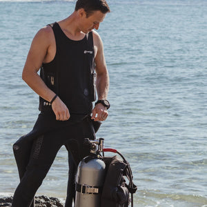 Black wrist remote controller by Venture Heat, worn on a man's left wrist in a black wetsuit by the ocean.