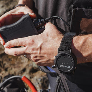 Black rugged wrist remote controller by Venture Heat, worn on a wrist and connected to a black power bank.