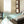 Black 29-inch Tower Circulator by Vornado, shown in a bedroom with blue air streams flowing over a bed.