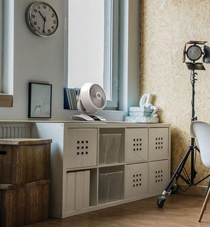 White small air circulator by Vornado with a spiral grill, positioned on a white shelf next to a window.