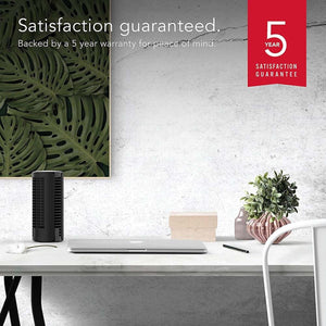 Black small oscillating tower fan by Vornado with vertical vents, on a modern white desk.