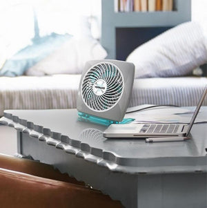 Grey personal air circulator by Vornado with white spiral grille and translucent blue base, on a grey table next to a laptop.