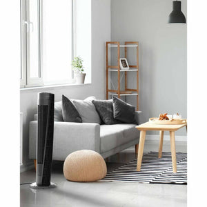 Black tower circulator by Vornado with a sleek, tall design and silver base, standing in a modern living room.