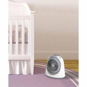 Ice white small nursery heater by Vornado with a gray fan grill and control buttons, on a purple rug next to a white crib.