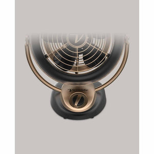 Vintage-style desk fan in gunmetal and antique brass by Vornado, front view showing the caged blades and control knob.