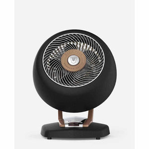 Black circular vintage whole room heater by Vornado with a metal grille and brown wood-look stand.