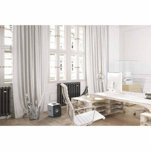 A stainless steel whole room heater by Vornado, compact and square with a black grille, on a light wooden floor in a modern office.