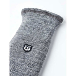 Grey merino wool five-finger liner glove by Hestra, featuring a black and white shield logo patch on the wrist.